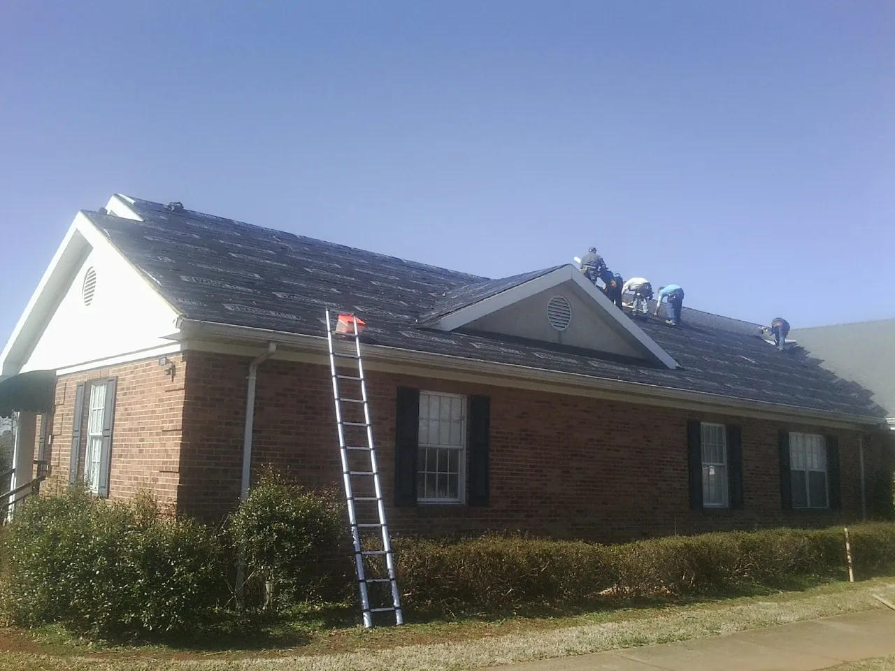 Crew tearing shingles off a brick ranch roof with a ladder set — Emergency Roof Repair work by our crew in Longview