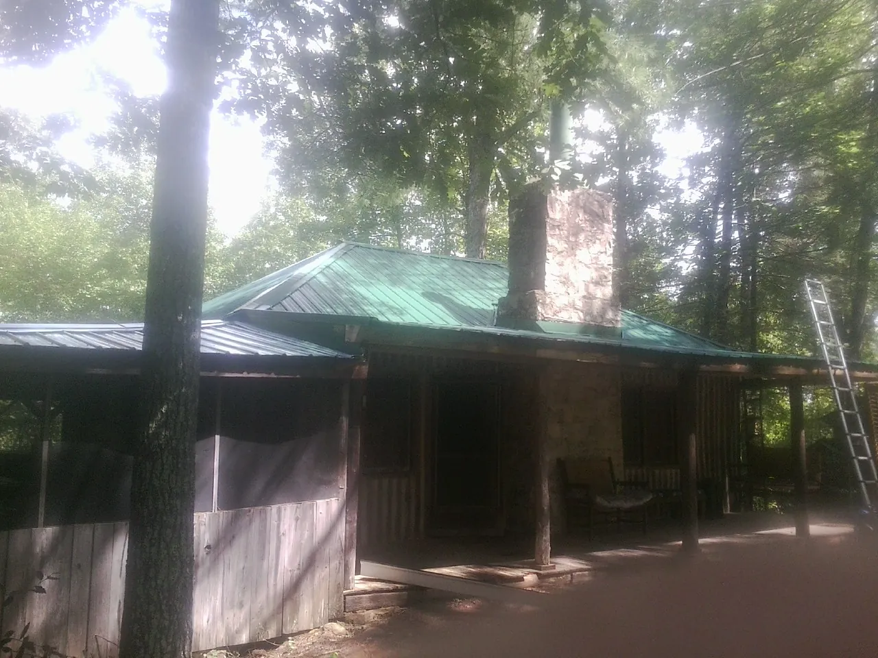 Green metal roof and stone chimney above a log cabin porch in Longview